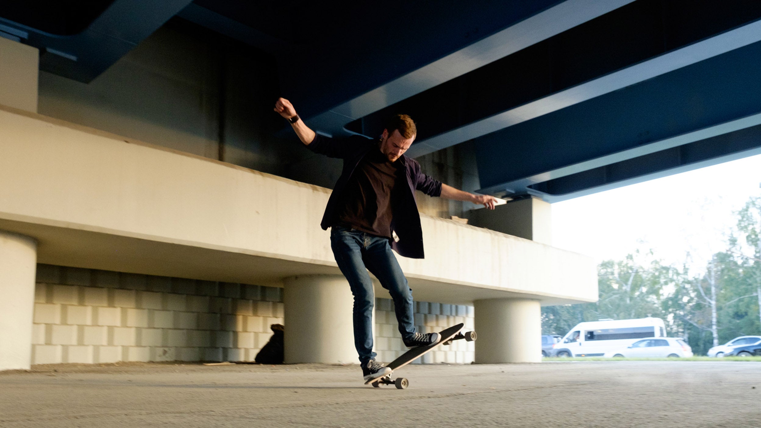 Man balancing on skateboard under bridge