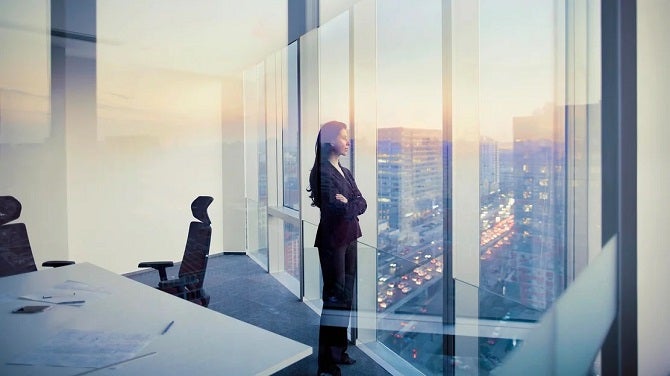 A business woman looking out the window in an office at sunset