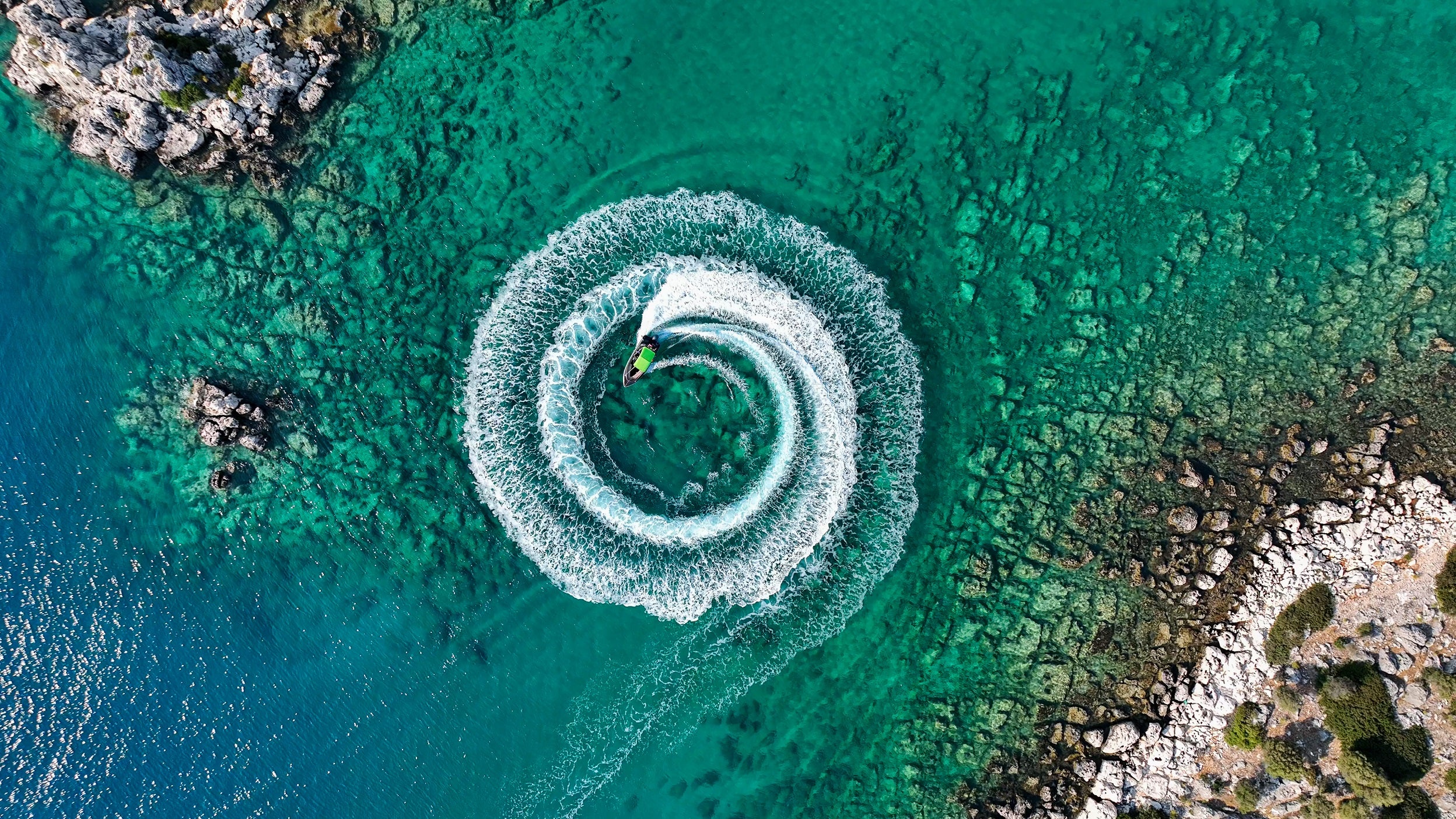 View from above of a jet ski driving in a spiral pattern in the ocean on a sunny day. 