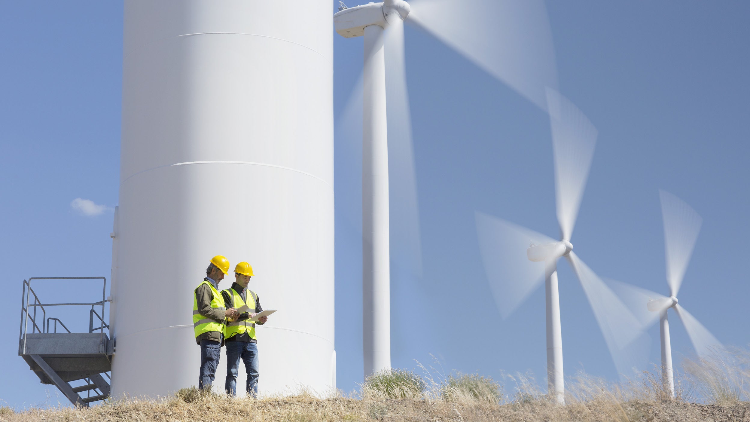Two men stand in front of wind turbines