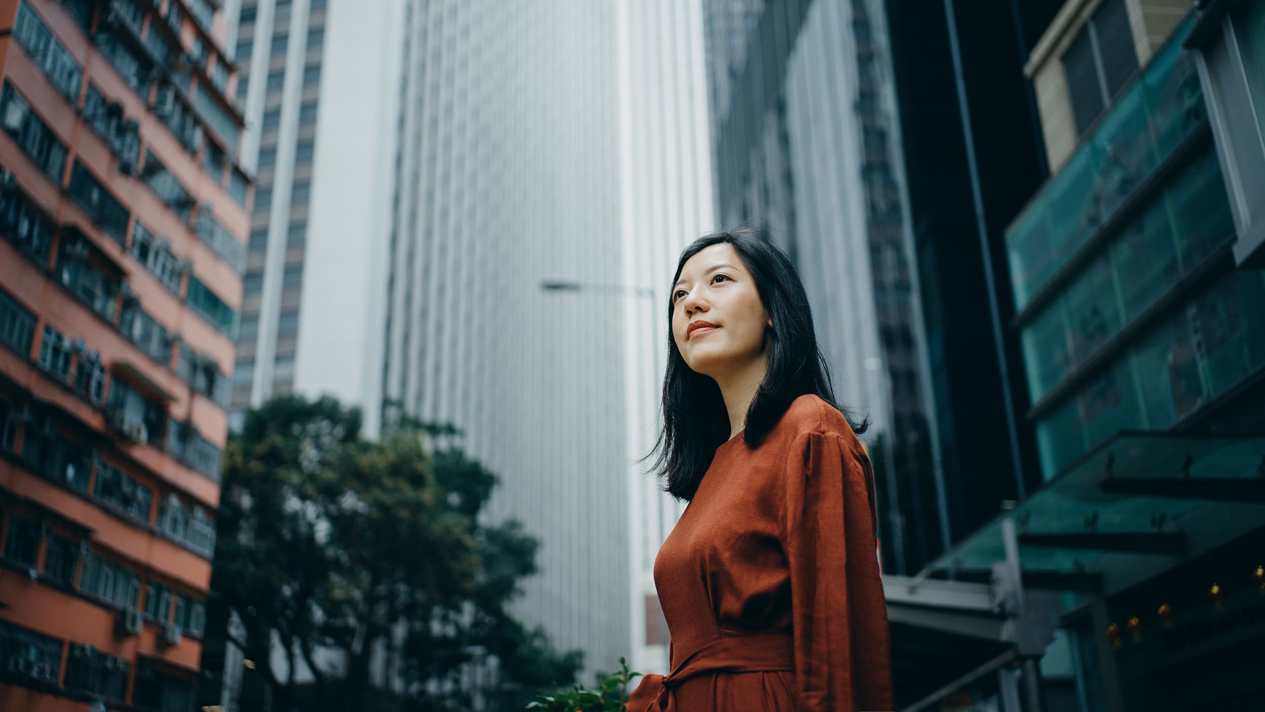 Low angle portrait of confidence young woman standing against highrise city buildings in city