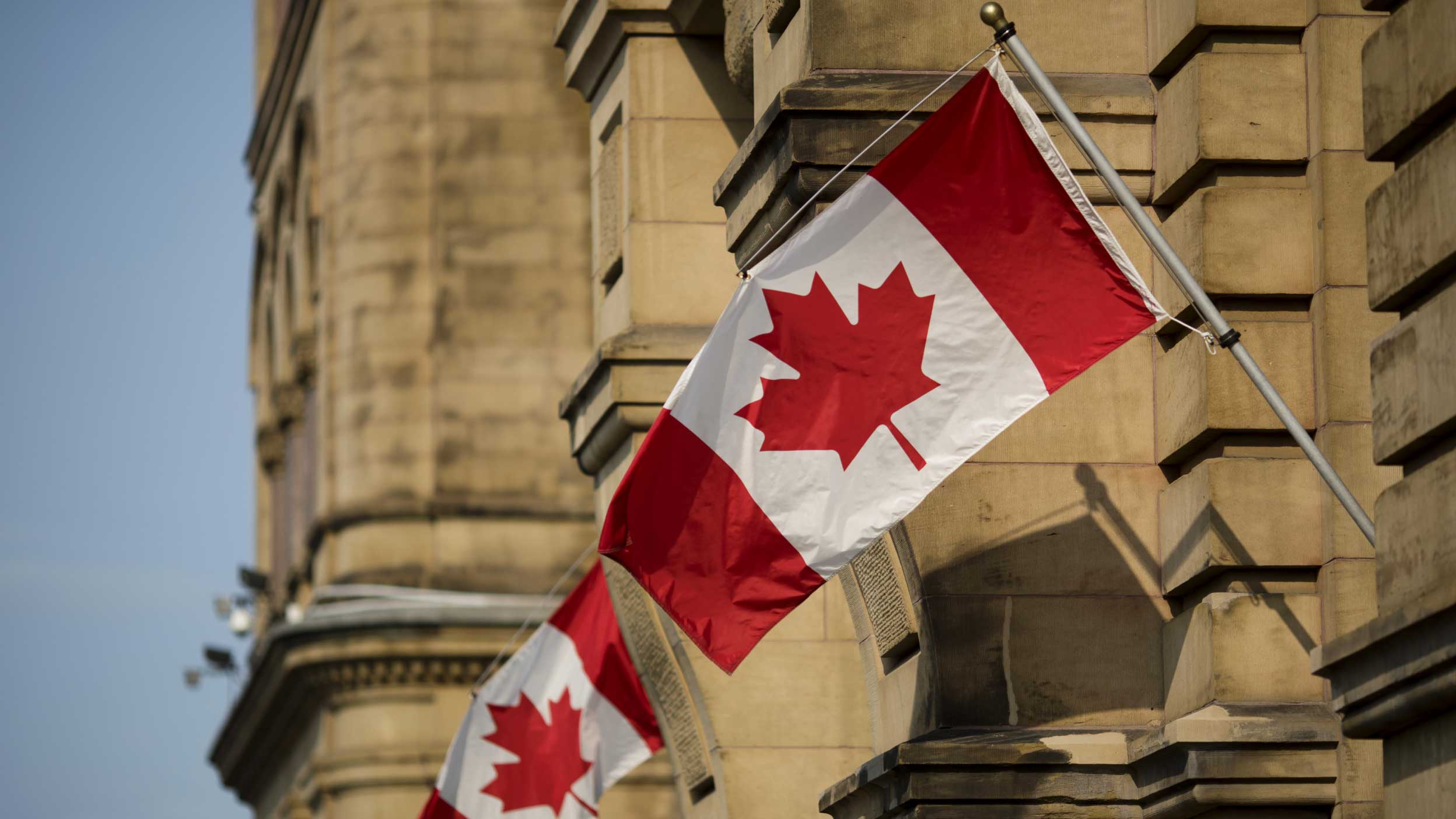 Canadian flags hang on display outside the Office of the Prime Minister and Privy Council building in Ottawa, Ontario, Canada. Photographer: Brent Lewin/Bloomberg