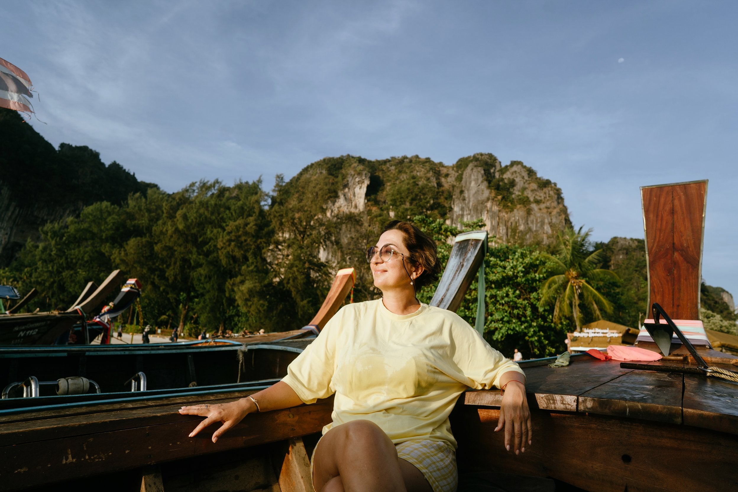 Happy beautiful woman of pre-retirement age in sunglasses and a yellow T-shirt sitting on board a wooden boat. Enjoying nature, the sea, the Phuket islands, Krabi province.