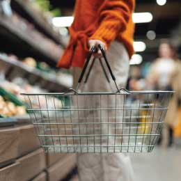 Lower section of young woman standing next to product aisle and choosing vegetables in the store. Young Asian woman doing grocery shopping in supermarket.