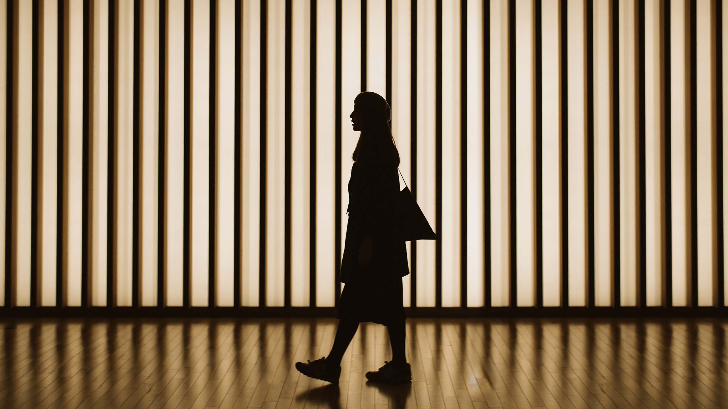 Silhouette d’une femme marchant devant un mur éclairé par des bandes 