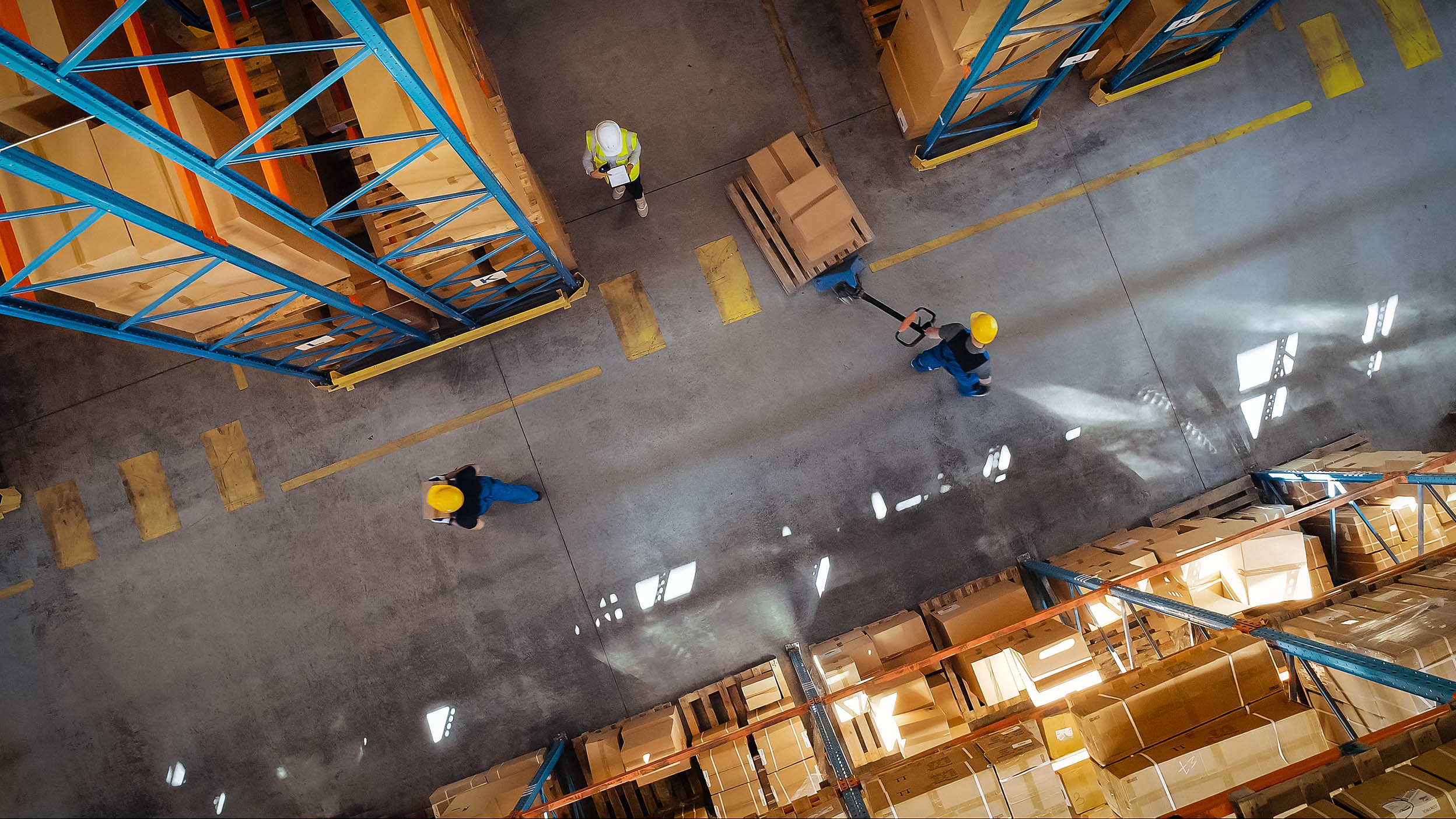 Forklift truck operator lifts pallet with cardboard box, as seen from above.