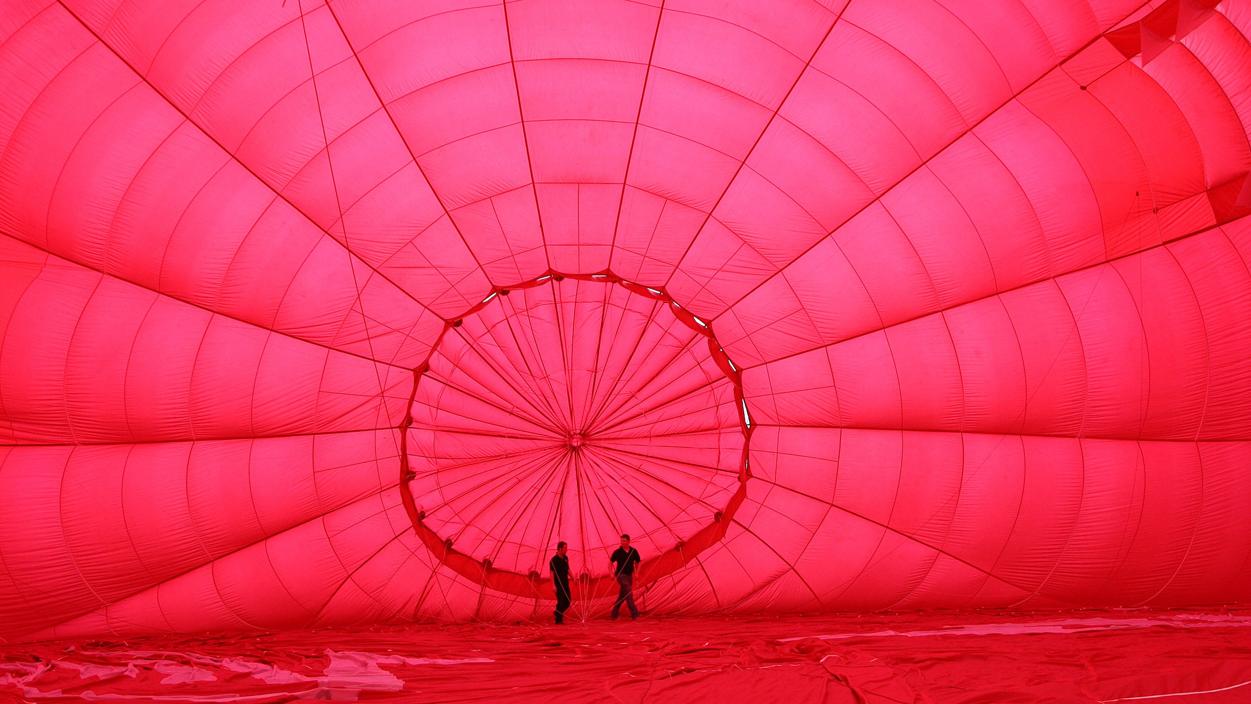 Ground crew prepare the inside of a red hot air balloon while it is pumped with cold air.