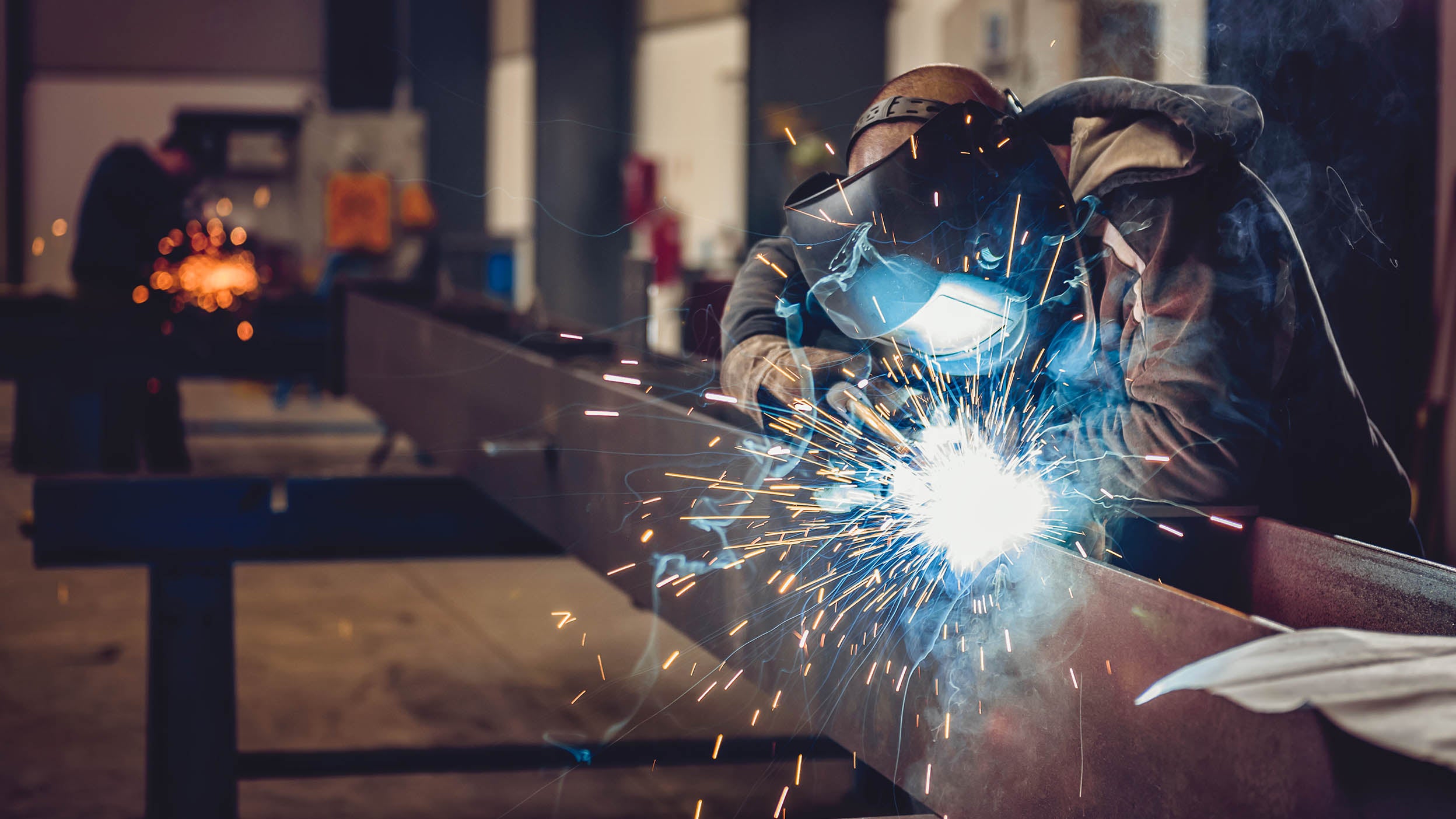 Industrial welder with torch and protective helmet in big hall welding metal profiles