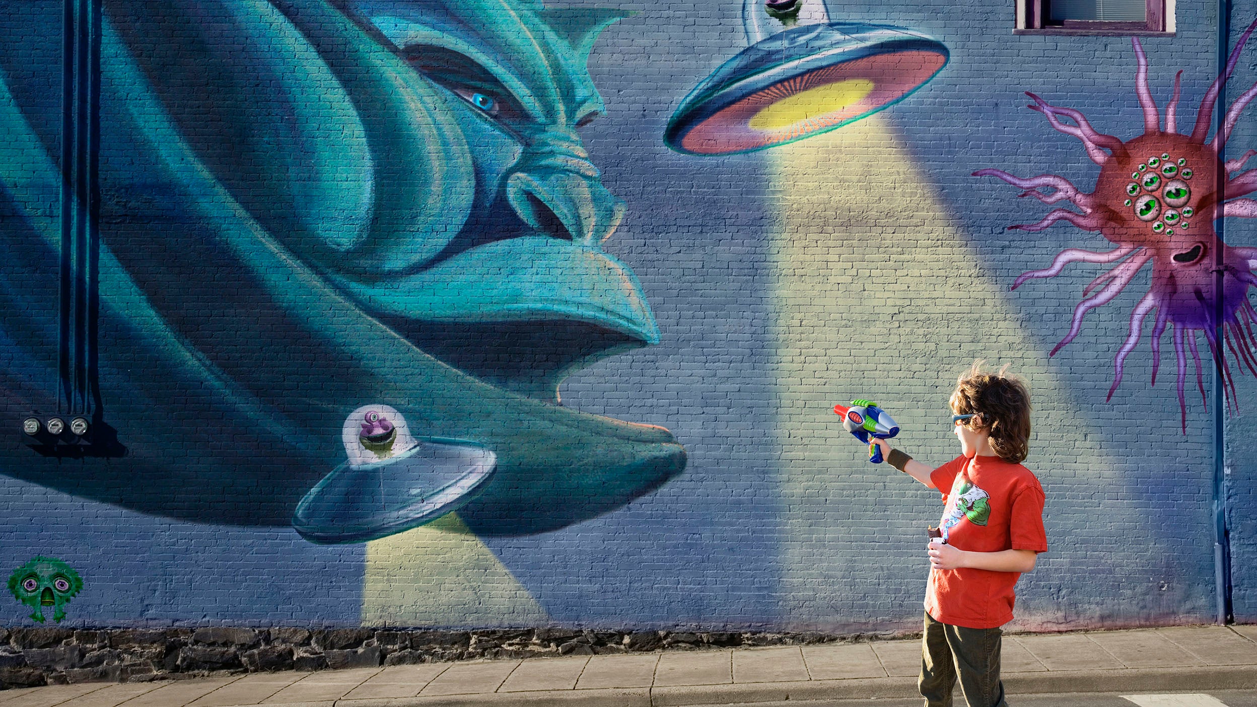 Boy shooting aliens painted on a wall mural with a pretend ray gun.