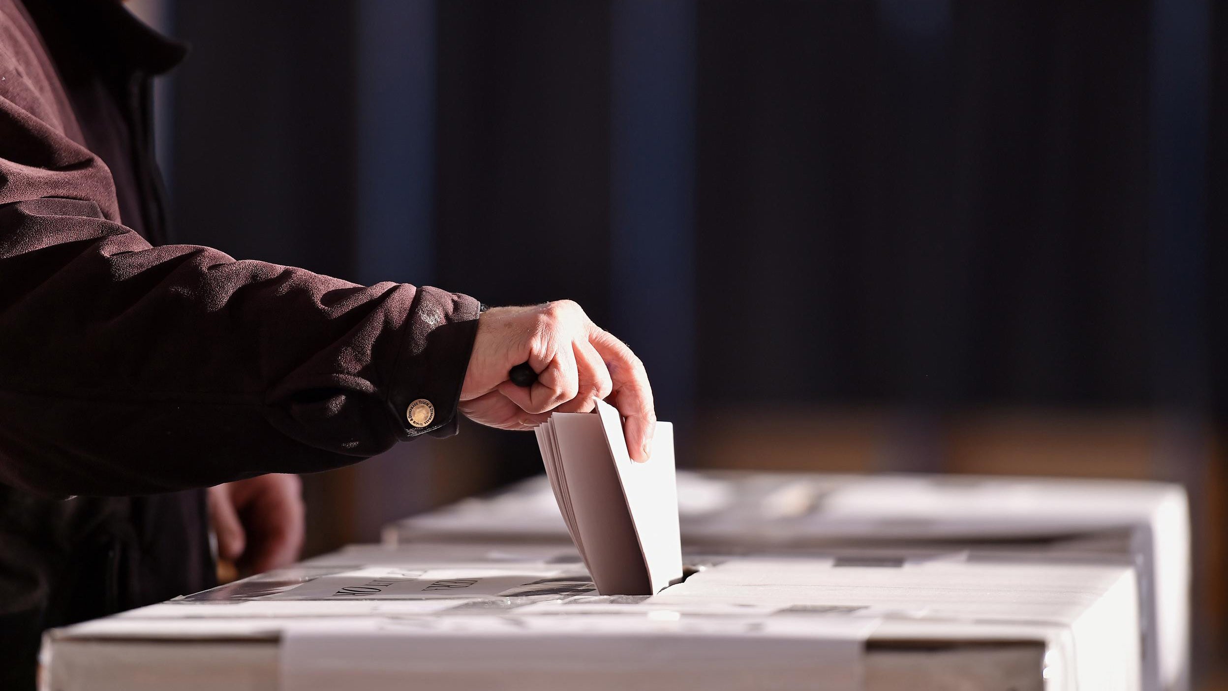 Hand of a person casting a vote into the ballot box during elections