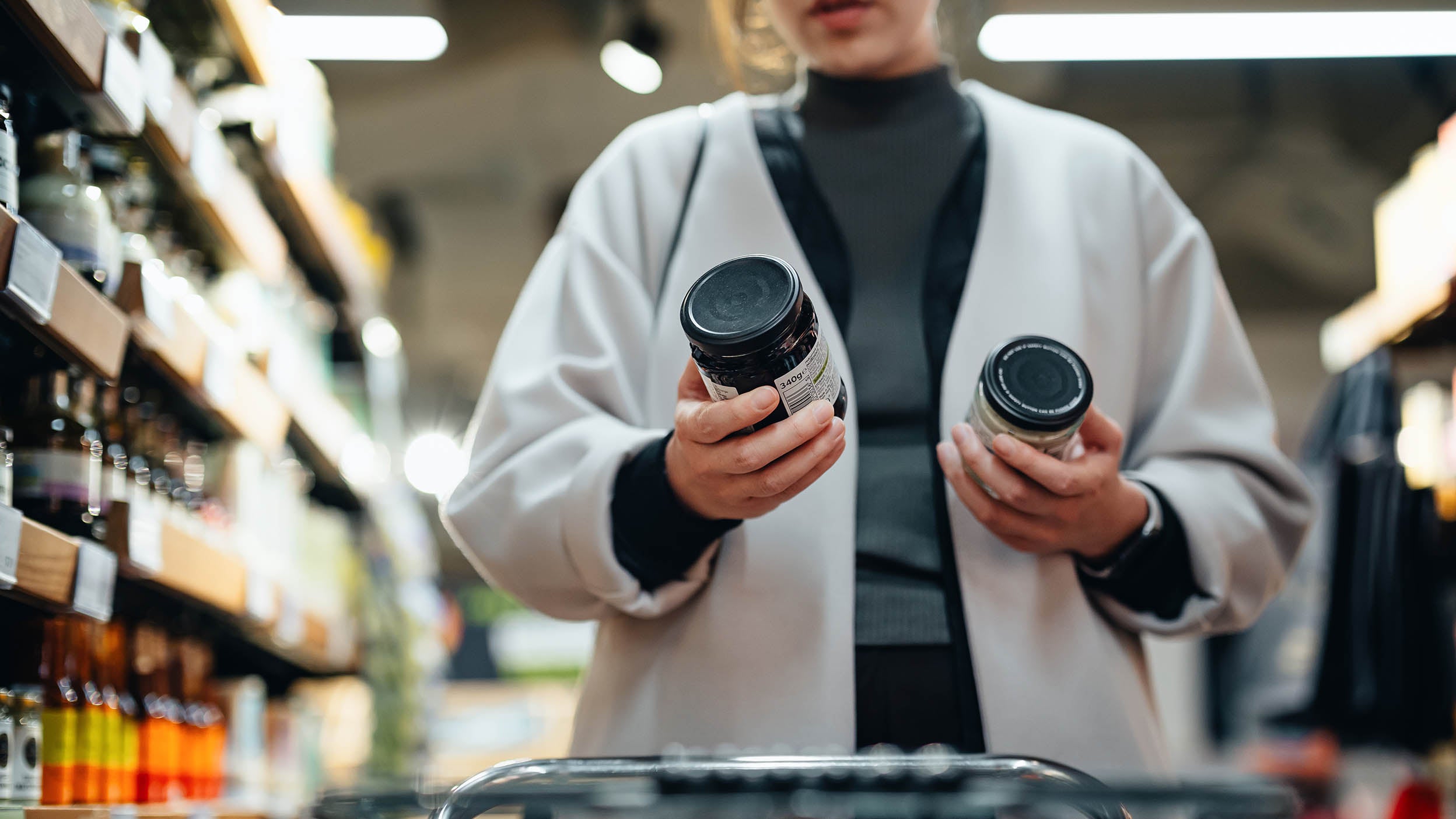 Woman with shopping cart shopping for sauce in supermarket.