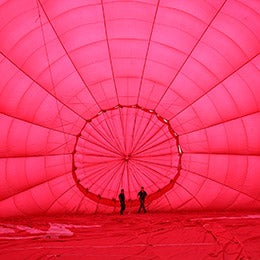 Ground%20crew%20prepare%20the%20inside%20of%20a%20red%20hot%20air%20balloon%20while%20it%20is%20pumped%20with%20cold%20air.