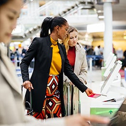 Two%20women%20check%20in%20for%20a%20flight%20at%20an%20airport%20kiosk.