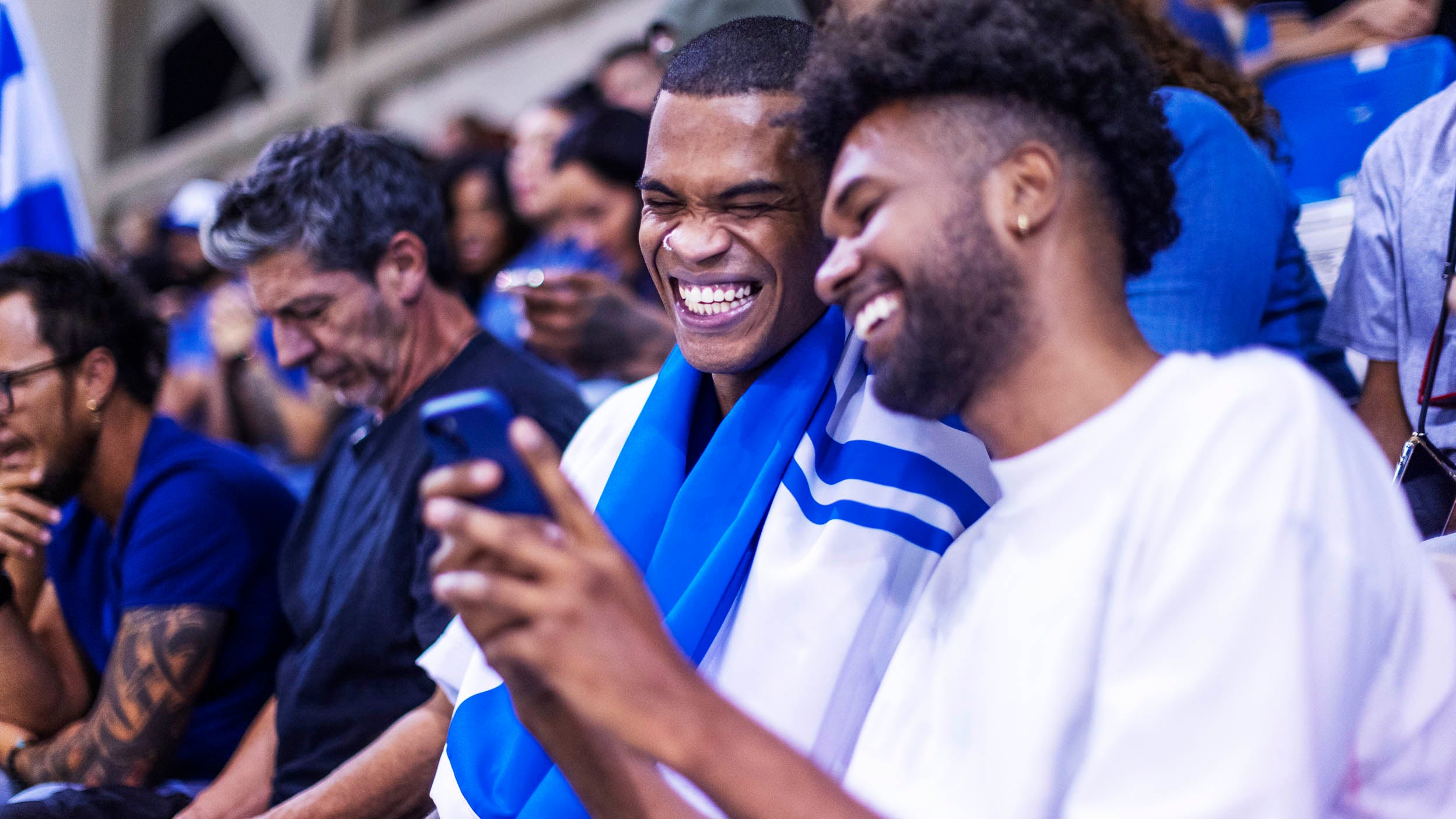 2 Fans in football jerseys look at a cell phone while at a sporting event. Invesco QQQ ETF holding companies are helping to enhance the in-stadium digital fan experience.