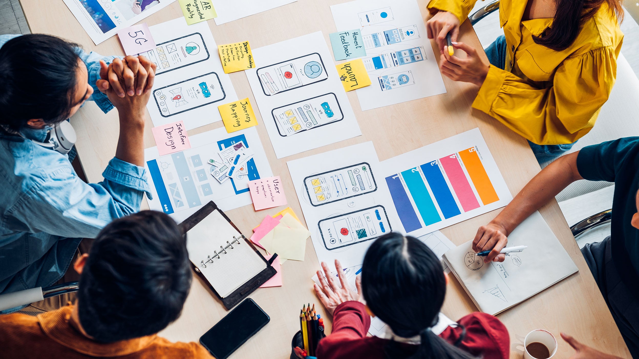  A group of people sat around a wooden table looking at design plans for a piece of technology. Invesco QQQ is an ETF that offers exposure to many technological innovations.