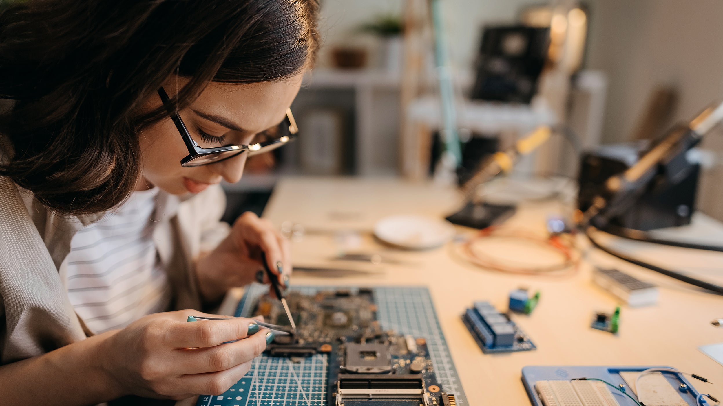 A women in glasses builds the motherboard of a GPU, a type of technology that powers many companies that are part of Invesco QQQ ETF.