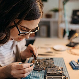 A women in glasses builds the motherboard of a GPU, a type of technology that powers many companies that are part of Invesco QQQ ETF.