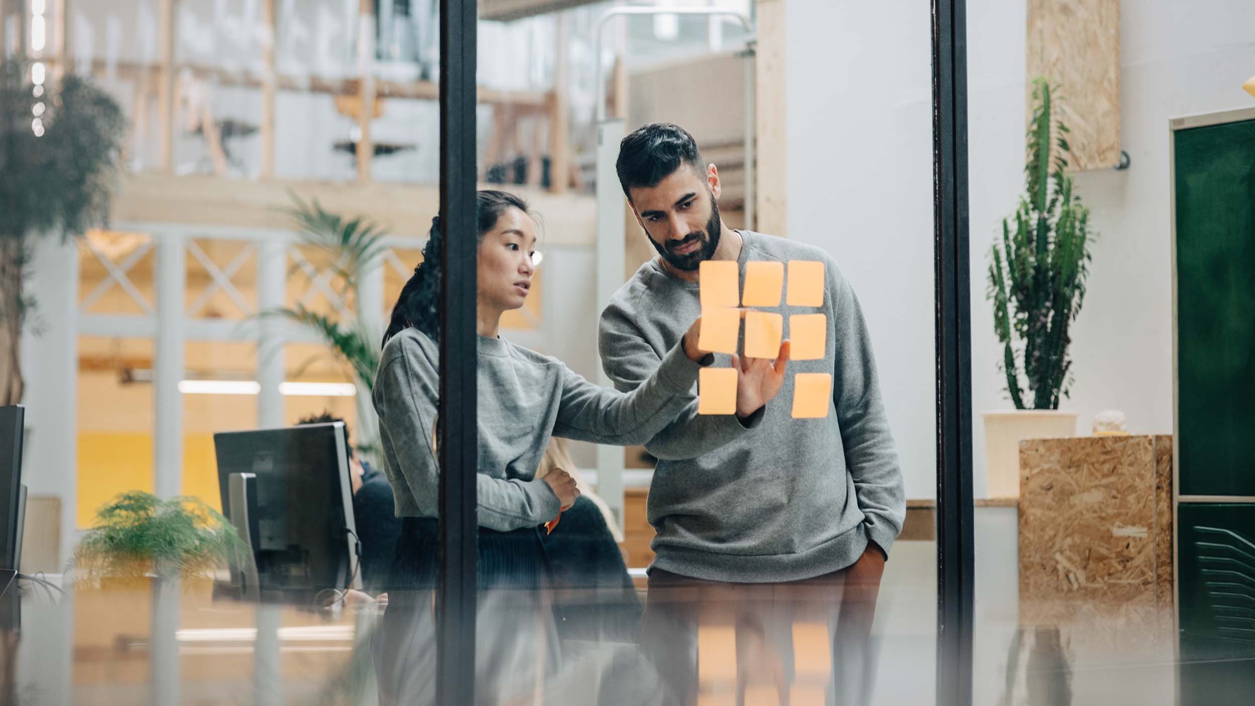 Businessman discussing with businesswoman sticking adhesive notes on glass wall in office