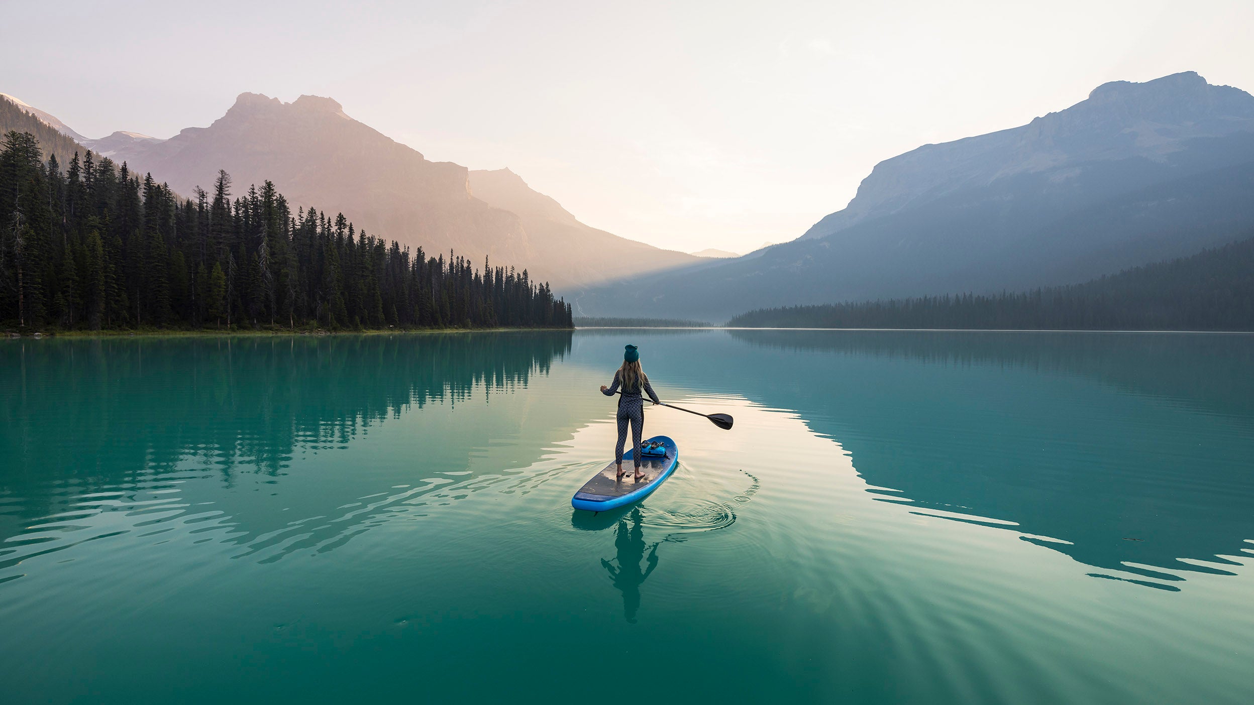 Woman standing on a paddle board in a lake looking at the mountains