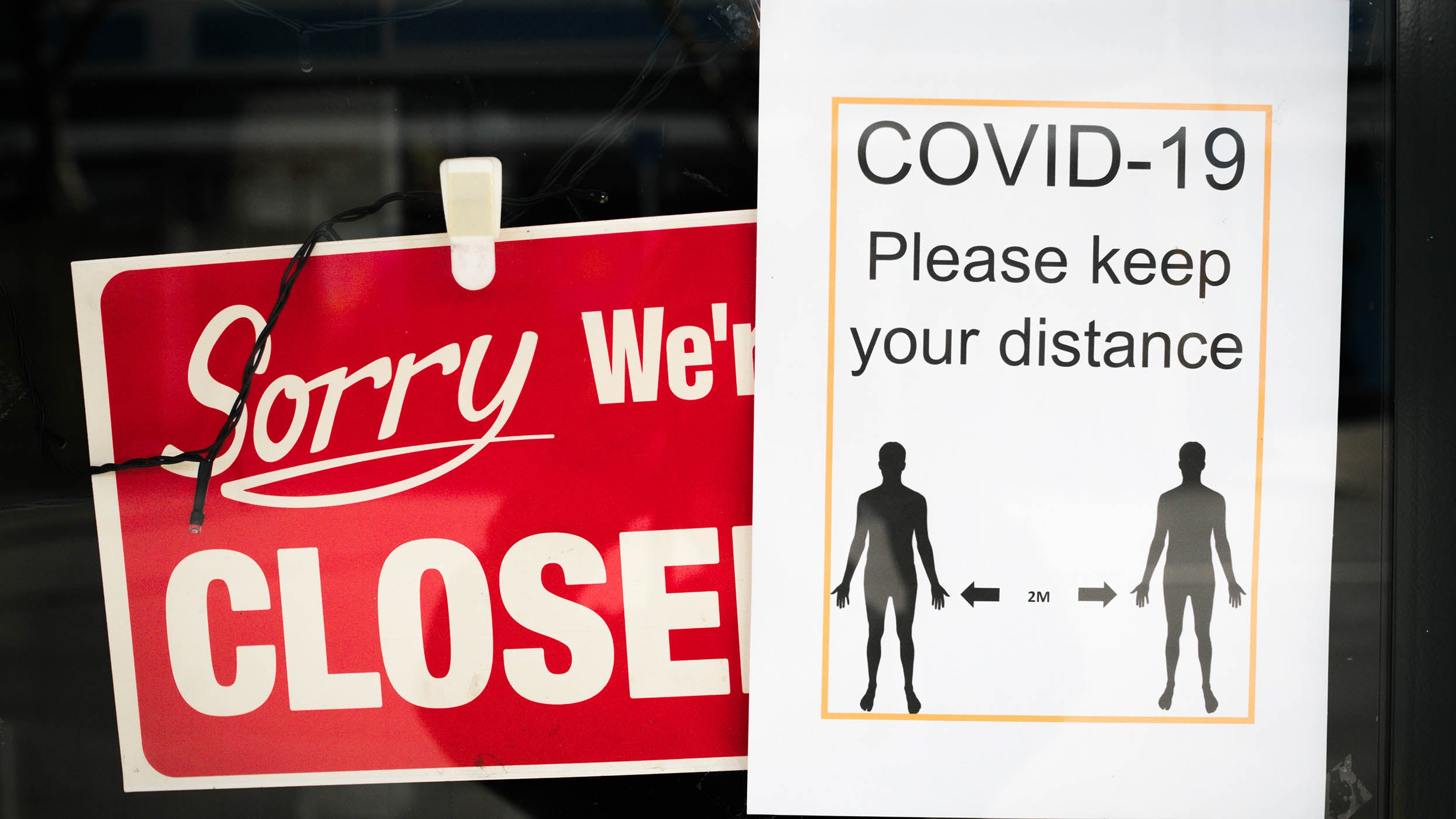 Signs in a store window saying that the shop is closed and to distance due to COVID.