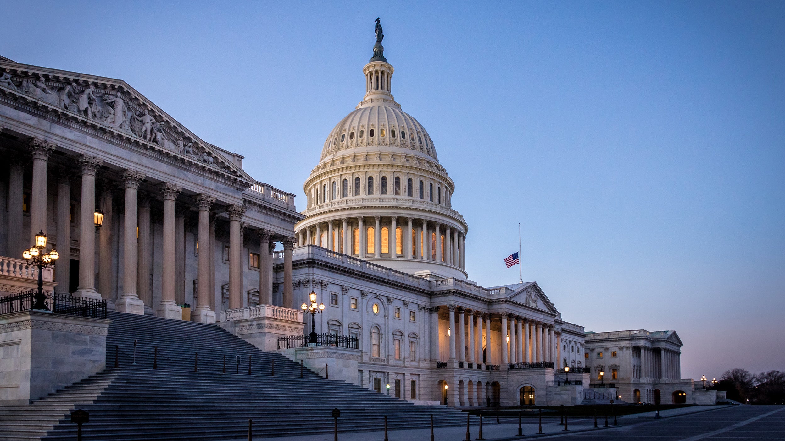 The US Capitol building at dusk with the American flag at half-staff.