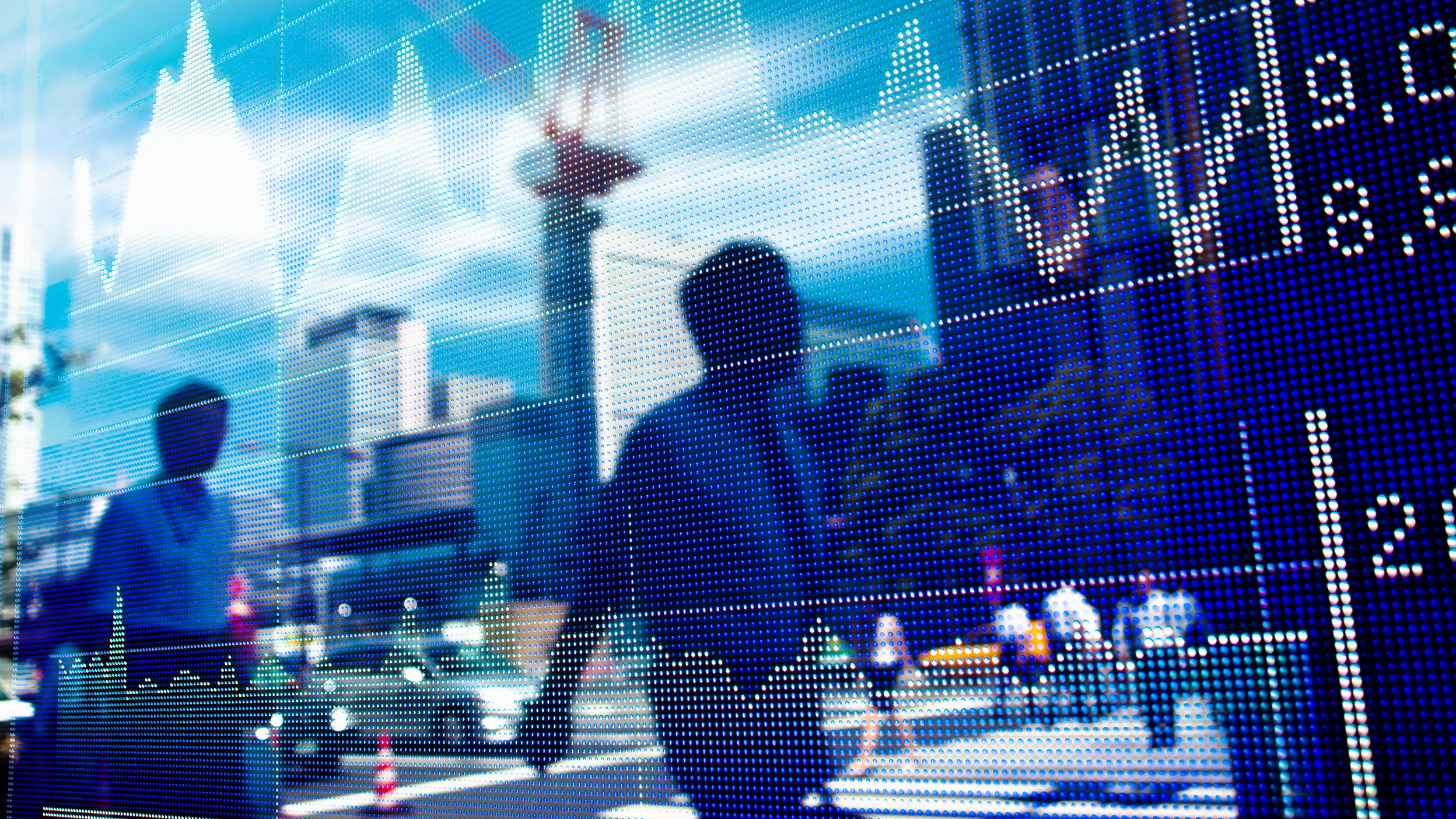 People’s reflections in a window as they walk past a stock market chart.